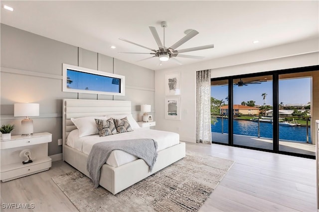 bedroom featuring ceiling fan, light hardwood / wood-style flooring, access to exterior, and a water view