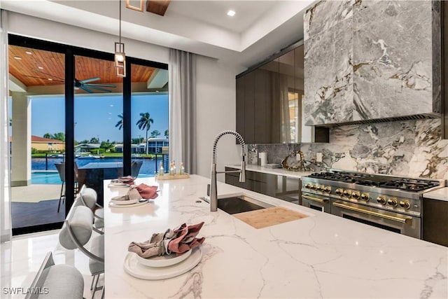 kitchen featuring light stone countertops, double oven range, sink, decorative light fixtures, and tasteful backsplash