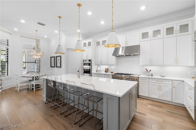 kitchen with decorative light fixtures, a kitchen island with sink, decorative backsplash, and white cabinetry