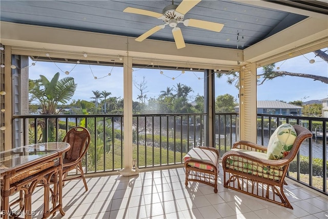 sunroom with ceiling fan and a water view