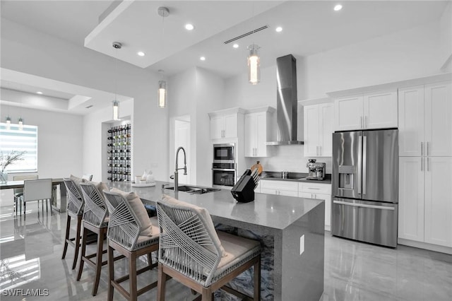 kitchen with dark stone counters, white cabinets, wall chimney range hood, appliances with stainless steel finishes, and a breakfast bar area