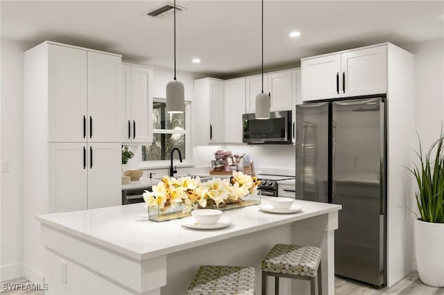 kitchen with a kitchen island, sink, hanging light fixtures, stainless steel appliances, and white cabinets