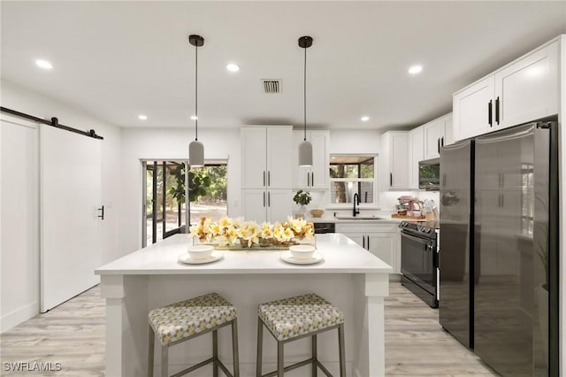 kitchen with white cabinetry, sink, stainless steel fridge, electric range, and a barn door