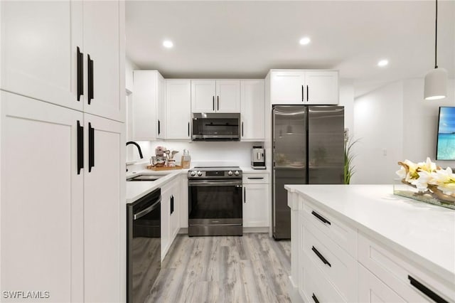 kitchen with appliances with stainless steel finishes, sink, white cabinetry, and pendant lighting