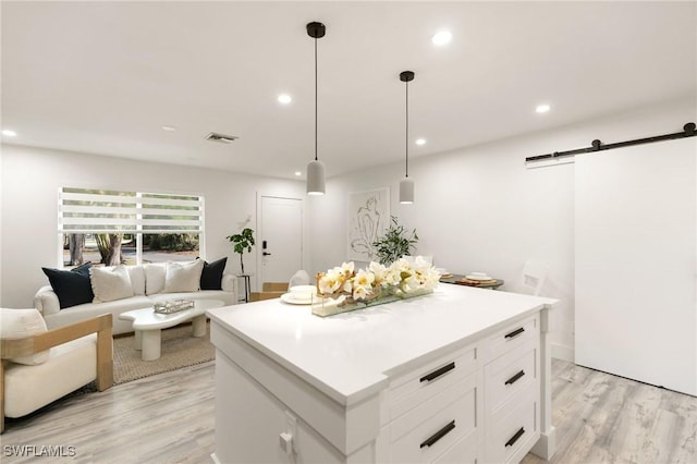 kitchen featuring white cabinetry, a barn door, decorative light fixtures, light hardwood / wood-style flooring, and a center island