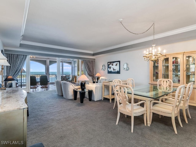 dining space with a raised ceiling, an inviting chandelier, dark colored carpet, ornamental molding, and a water view