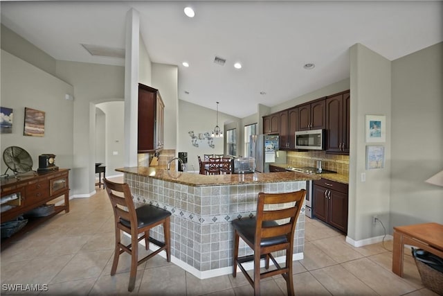 kitchen featuring kitchen peninsula, pendant lighting, lofted ceiling, a breakfast bar area, and appliances with stainless steel finishes