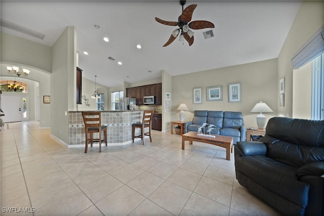 tiled living room with ceiling fan with notable chandelier and vaulted ceiling