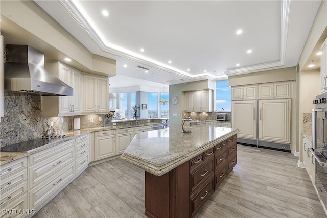 kitchen featuring black electric stovetop, tasteful backsplash, a tray ceiling, wall chimney range hood, and a kitchen island