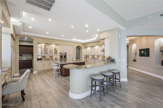 kitchen with light stone countertops, a kitchen breakfast bar, light wood-type flooring, tasteful backsplash, and oven