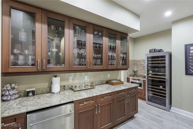 bar with light stone countertops, stainless steel dishwasher, dark brown cabinetry, beverage cooler, and light hardwood / wood-style flooring