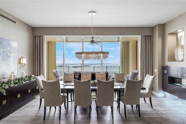 dining room with wood-type flooring, ceiling fan with notable chandelier, and a water view