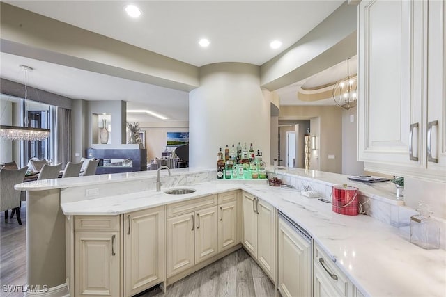 kitchen featuring kitchen peninsula, light stone counters, hanging light fixtures, and sink