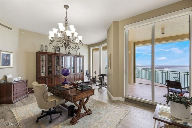 home office with a notable chandelier, a water view, and light wood-type flooring