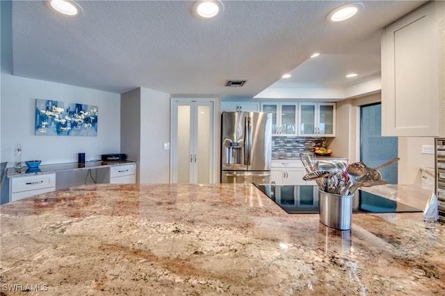 kitchen featuring stainless steel fridge with ice dispenser, a textured ceiling, tasteful backsplash, light stone counters, and white cabinetry