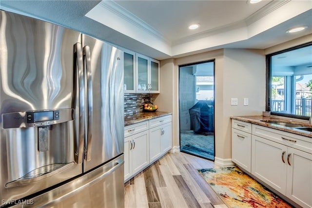 kitchen featuring decorative backsplash, stainless steel fridge, a tray ceiling, dark stone countertops, and white cabinetry