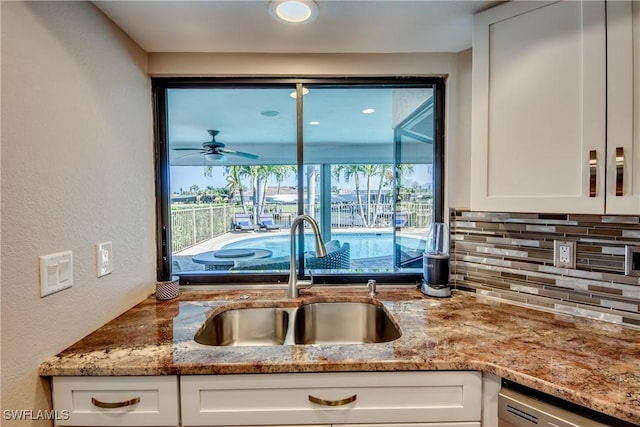 kitchen with light stone counters, sink, white cabinets, and stainless steel dishwasher