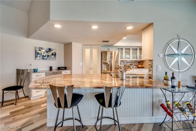 kitchen featuring white cabinets, decorative backsplash, stainless steel fridge, light stone counters, and kitchen peninsula