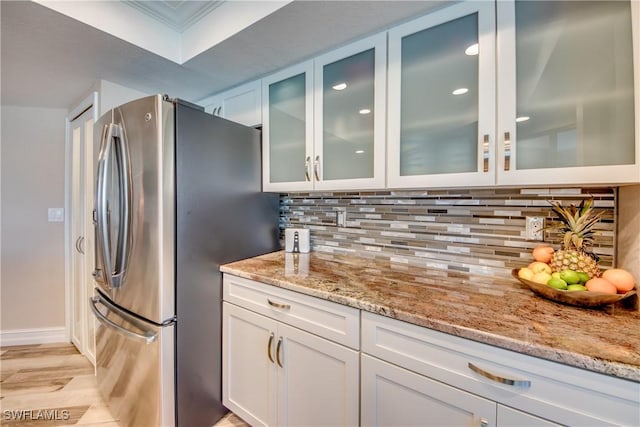 kitchen with stainless steel refrigerator, light stone countertops, white cabinets, and decorative backsplash