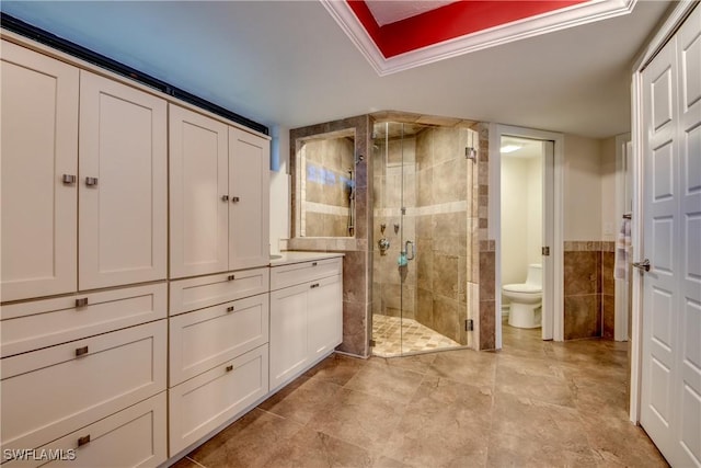 bathroom featuring crown molding, a shower with door, tile walls, and toilet