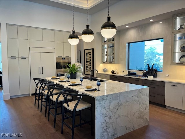 kitchen featuring pendant lighting, an island with sink, sink, dark hardwood / wood-style flooring, and paneled built in fridge