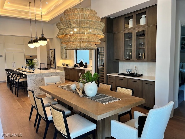 dining space with sink, a towering ceiling, light hardwood / wood-style flooring, and a raised ceiling