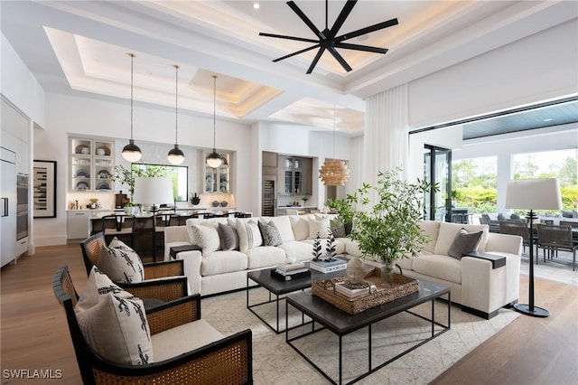 living room featuring a towering ceiling, light wood-style floors, plenty of natural light, and a tray ceiling