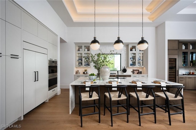 kitchen featuring a raised ceiling, light wood-type flooring, a kitchen bar, and a center island with sink