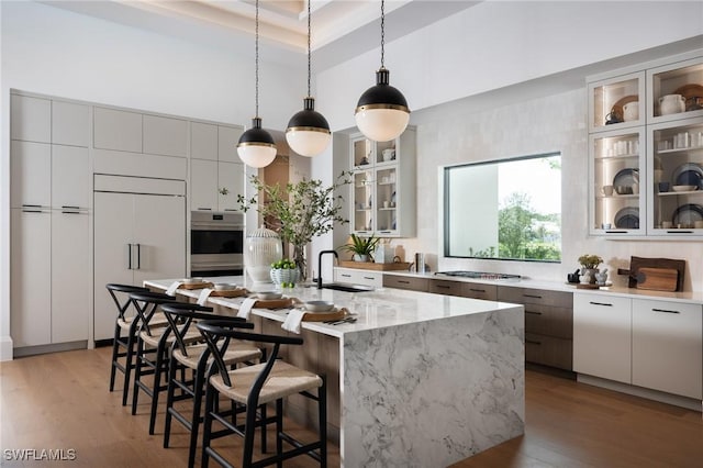 kitchen featuring paneled built in fridge, stainless steel oven, a sink, modern cabinets, and a kitchen breakfast bar