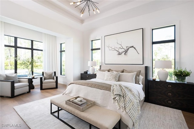 bedroom with a notable chandelier, a raised ceiling, and wood finished floors