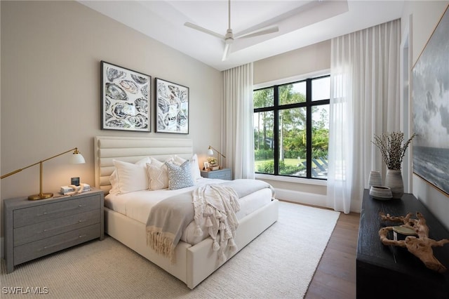 bedroom featuring a raised ceiling, ceiling fan, and light wood finished floors