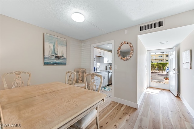 dining space with a textured ceiling, light hardwood / wood-style floors, and sink