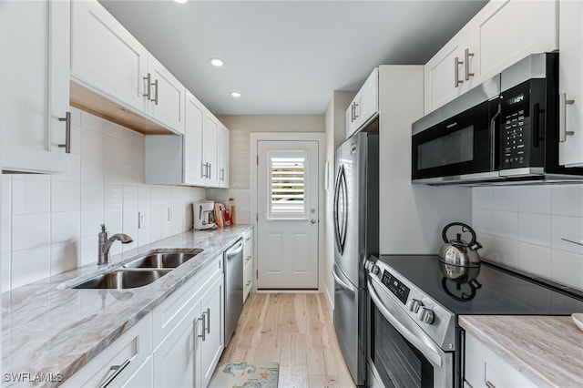 kitchen featuring white cabinets, stainless steel appliances, light stone countertops, and sink