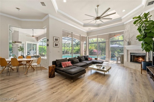 living room with a high ceiling, ornamental molding, ceiling fan, a premium fireplace, and light wood-type flooring