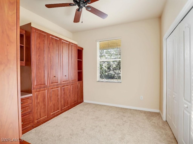 unfurnished bedroom featuring ceiling fan, light colored carpet, and multiple closets