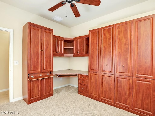 unfurnished office featuring light colored carpet, ceiling fan, and built in desk