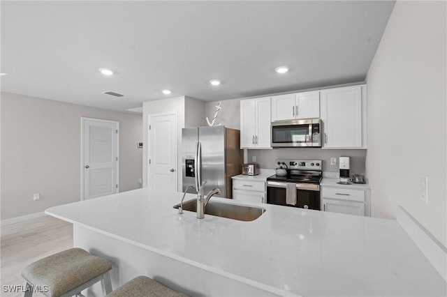 kitchen with appliances with stainless steel finishes, a breakfast bar, sink, and white cabinets