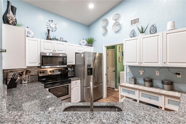 kitchen with white cabinets, appliances with stainless steel finishes, and dark stone counters