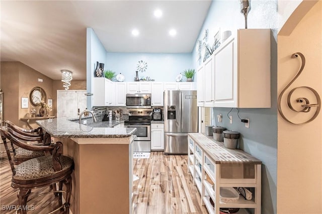 kitchen with kitchen peninsula, appliances with stainless steel finishes, white cabinets, and a breakfast bar area