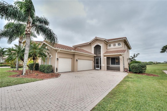 mediterranean / spanish-style house featuring a tiled roof, an attached garage, decorative driveway, a front yard, and stucco siding