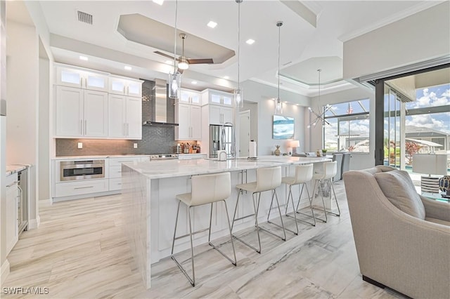 kitchen with pendant lighting, white cabinetry, a spacious island, a tray ceiling, and wall chimney exhaust hood