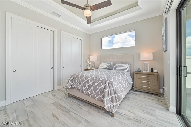 bedroom featuring ceiling fan, ornamental molding, a raised ceiling, and two closets