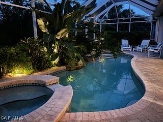 view of pool featuring an in ground hot tub, a patio area, and glass enclosure