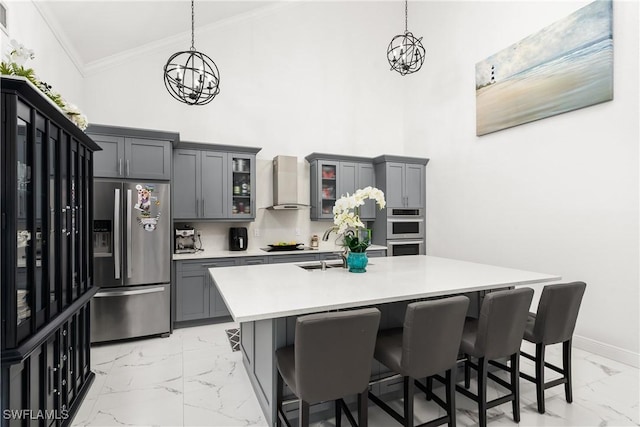 kitchen with stainless steel appliances, a chandelier, hanging light fixtures, and wall chimney range hood