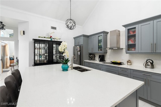 kitchen with gray cabinets, pendant lighting, sink, stainless steel fridge, and wall chimney exhaust hood