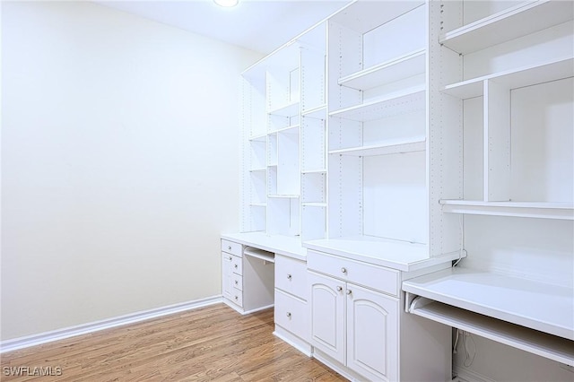 spacious closet with light hardwood / wood-style flooring and built in desk