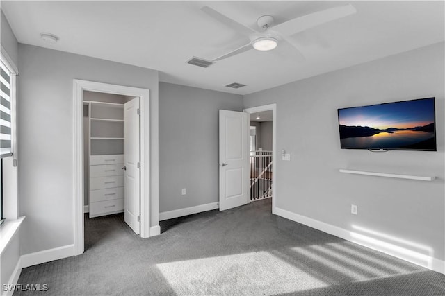 unfurnished bedroom featuring ceiling fan, a spacious closet, a closet, and dark colored carpet