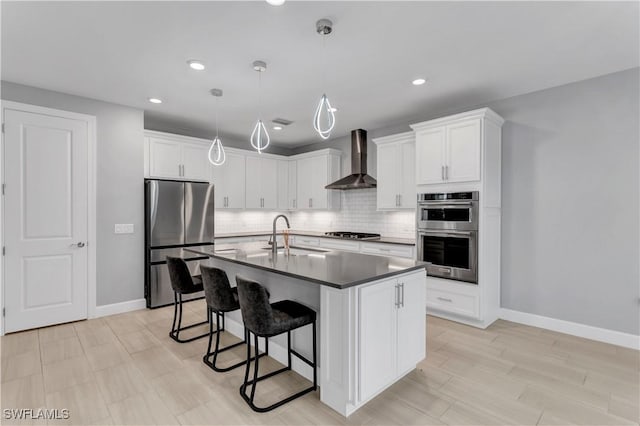 kitchen featuring wall chimney range hood, pendant lighting, sink, stainless steel appliances, and white cabinets