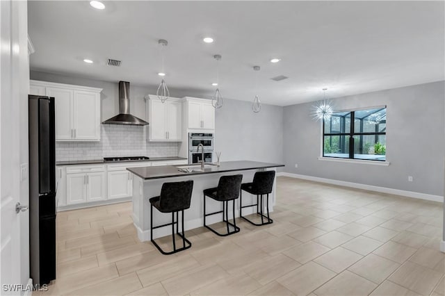 kitchen with a center island with sink, black refrigerator, wall chimney range hood, pendant lighting, and white cabinets