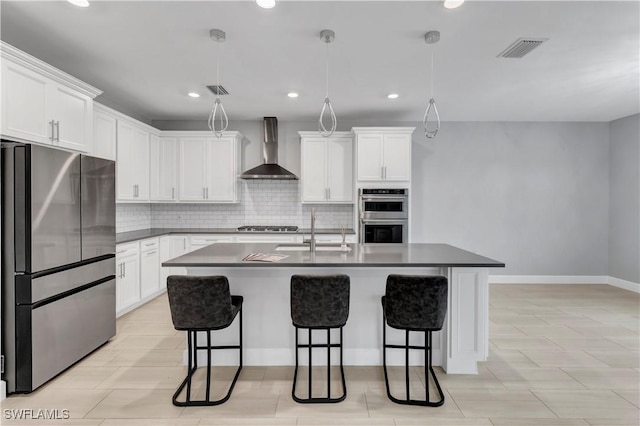 kitchen featuring stainless steel appliances, hanging light fixtures, wall chimney exhaust hood, white cabinets, and sink